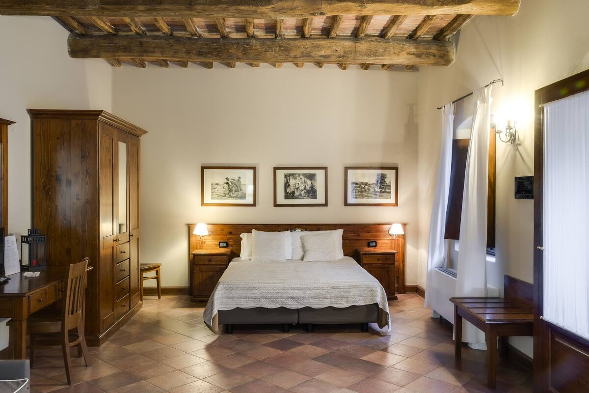 A bedroom with a wooden bed, a desk, and a wardrobe. There are three framed pictures on the wall.