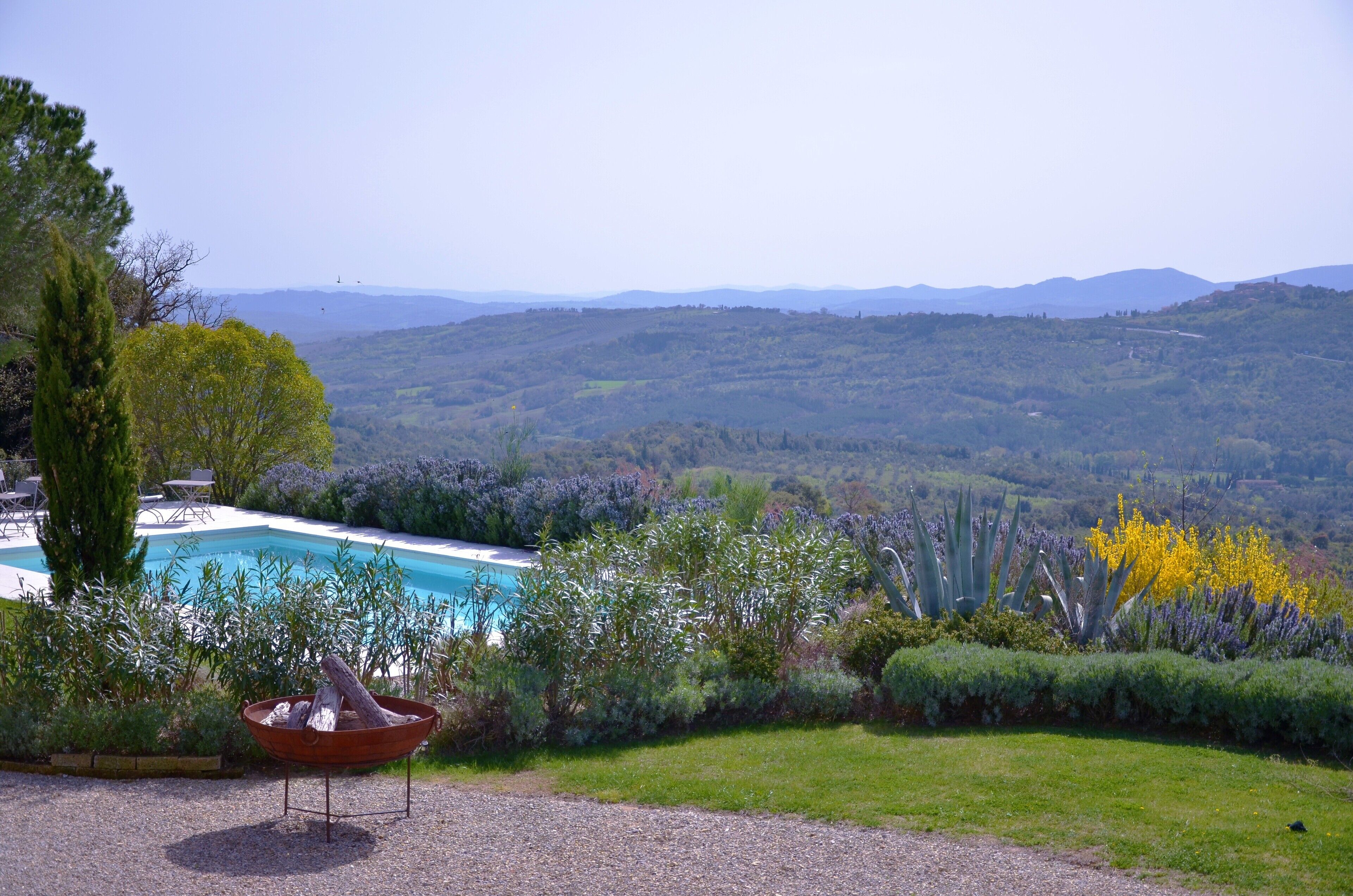 A pool with a view of mountains, surrounded by greenery and a wooden tub.