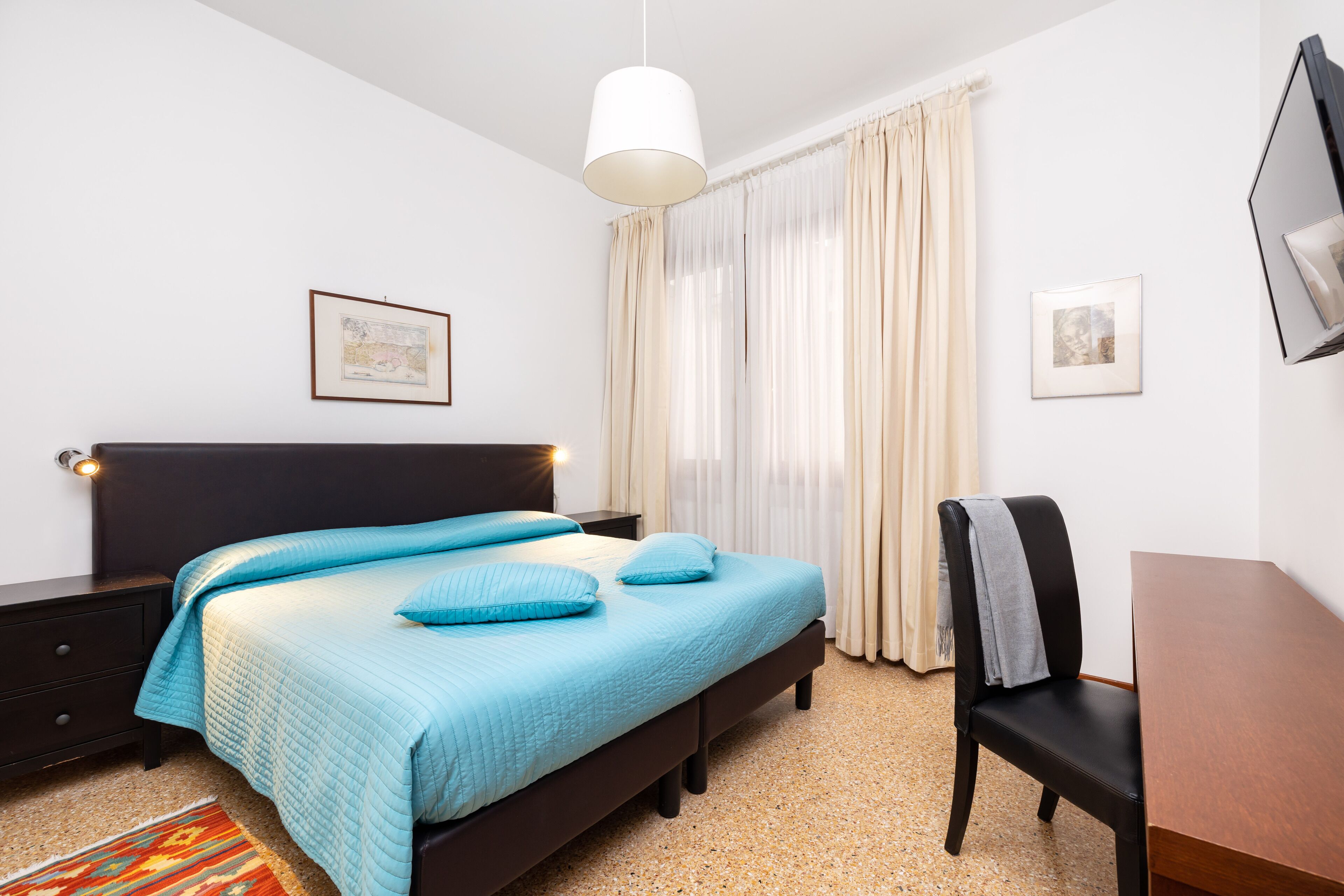 Une chambre à coucher comprenant un lit, un bureau, une chaise, une table de chevet, une lampe et un téléviseur fixé au mur.
