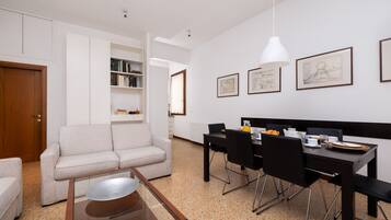 A modern living room with a sofa, a dining table with chairs, and a kitchen area with cabinets and a refrigerator.
