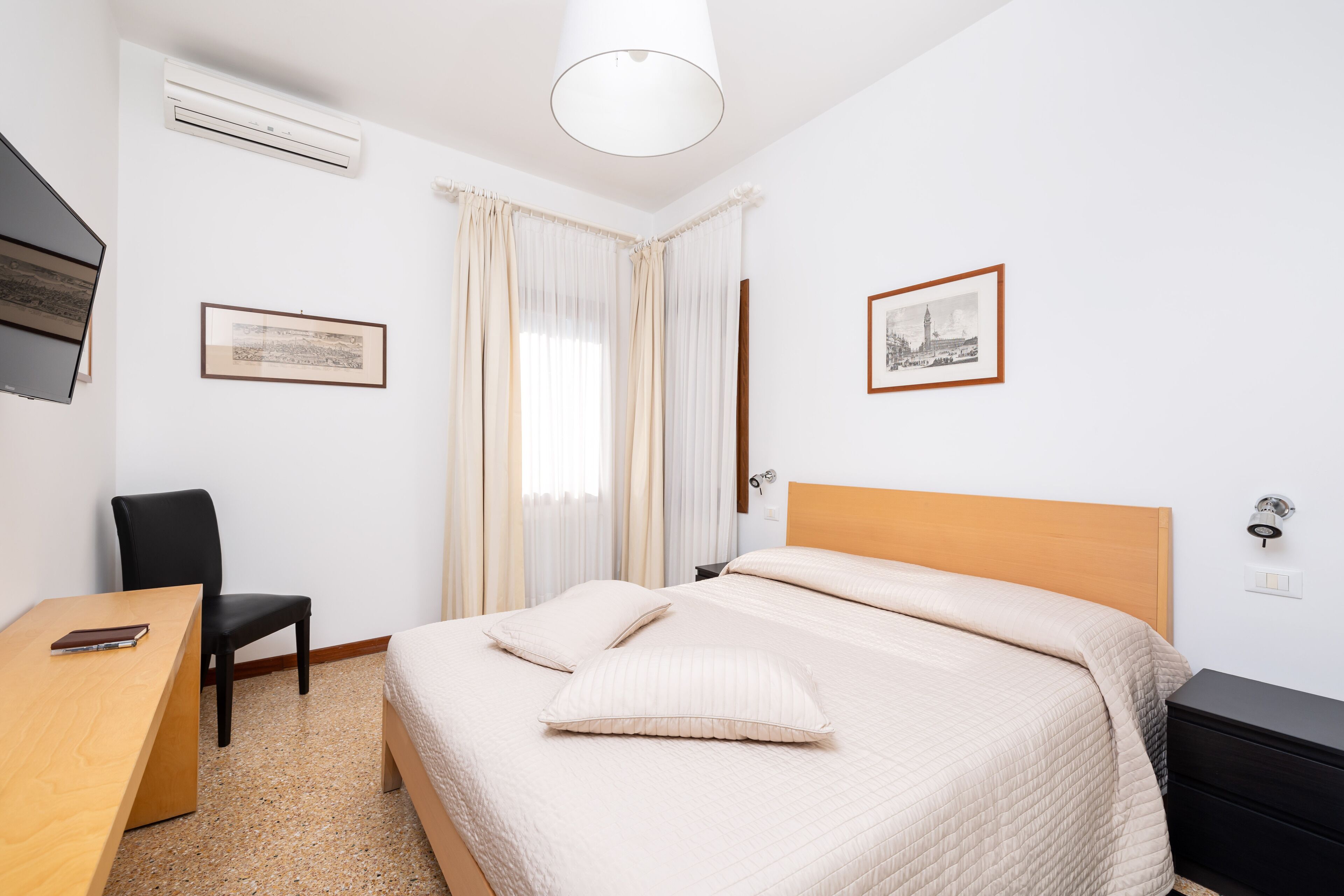 A hotel room with a bed, a desk, a chair, and a TV.