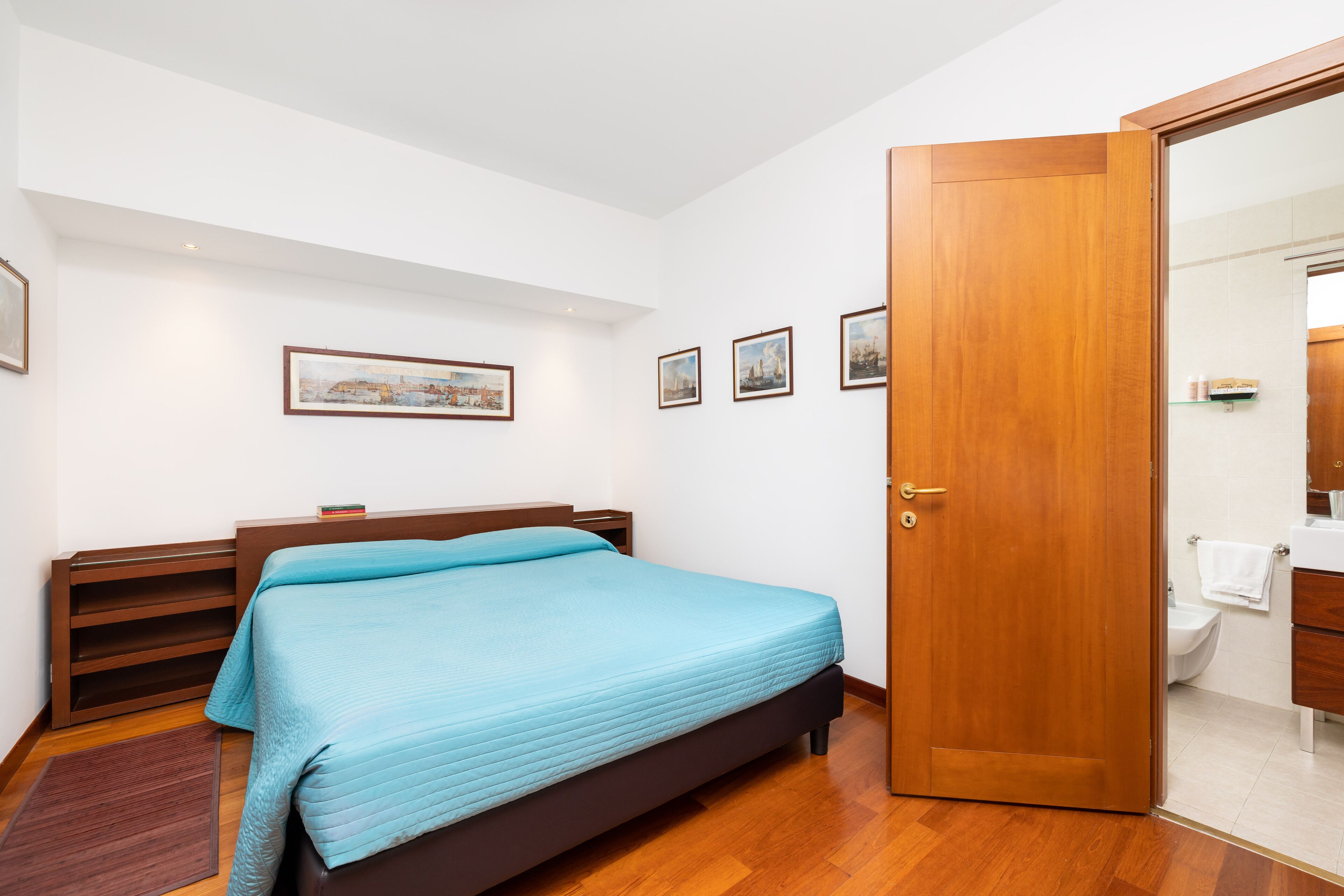 Un dormitorio con cama, cabecero de madera, una mesita de noche y un baño visible a través de una puerta abierta.