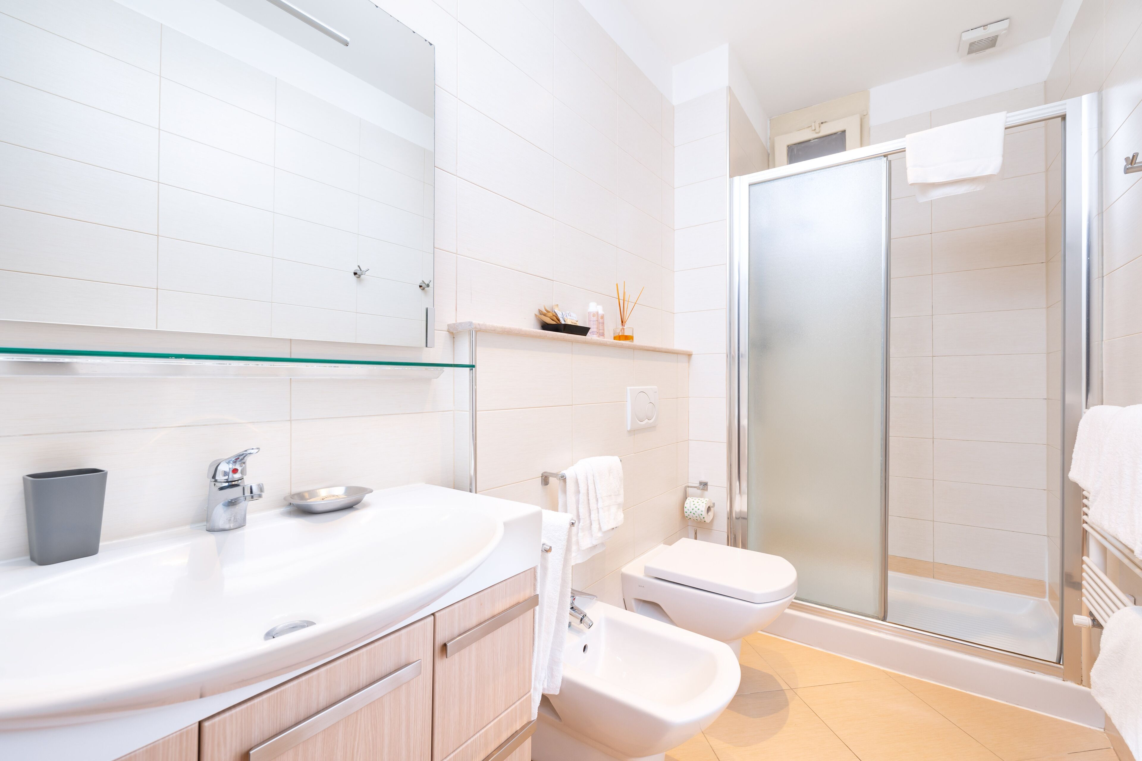 A modern bathroom with a large mirror, a sink, a bidet, and a glass-enclosed shower.