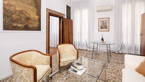 A living room with a sofa, two armchairs, a glass coffee table, a dining table with chairs, and a painting on the wall. - Ca' Foscolo Residence (Venice)