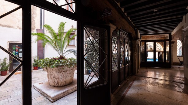 A reception area with a large potted plant, a reception desk, and a view of the outside courtyard. - Ca' Foscolo Residence (Venice)