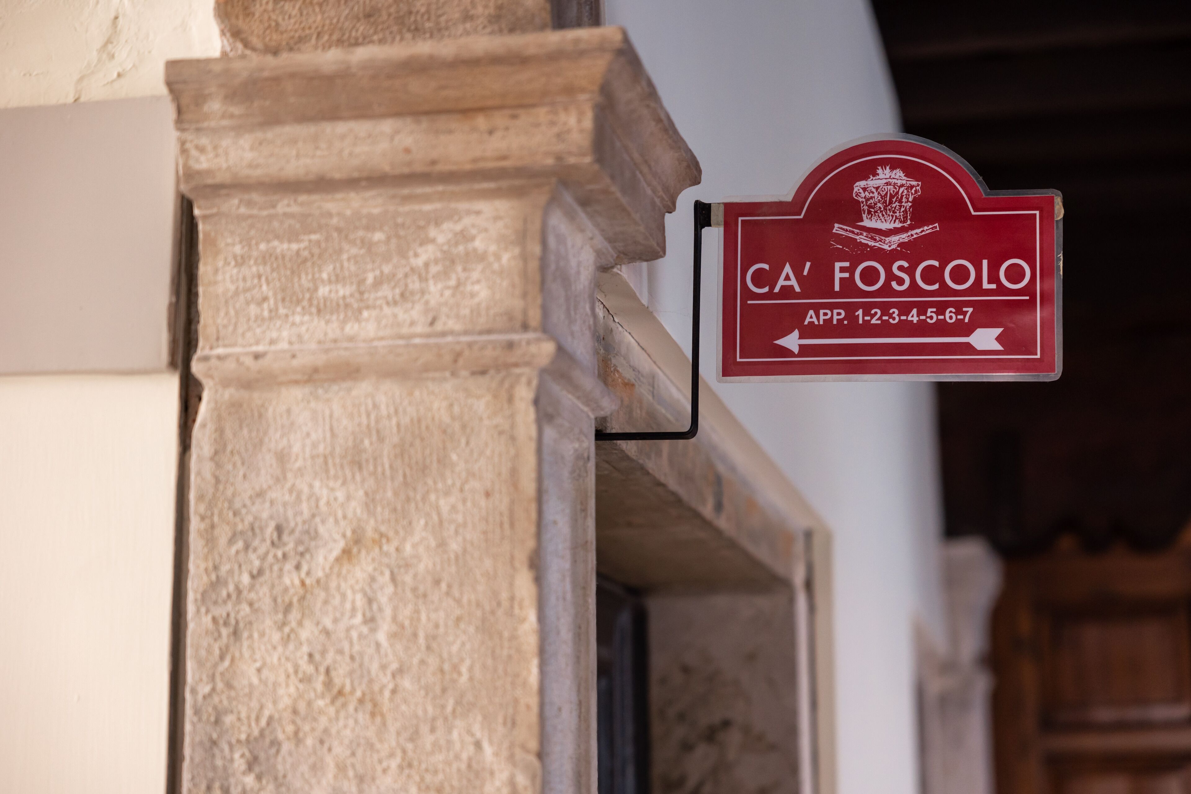 Un pilar de piedra con un letrero rojo que indica 'CA' FOSCOLO' y una flecha direccional.