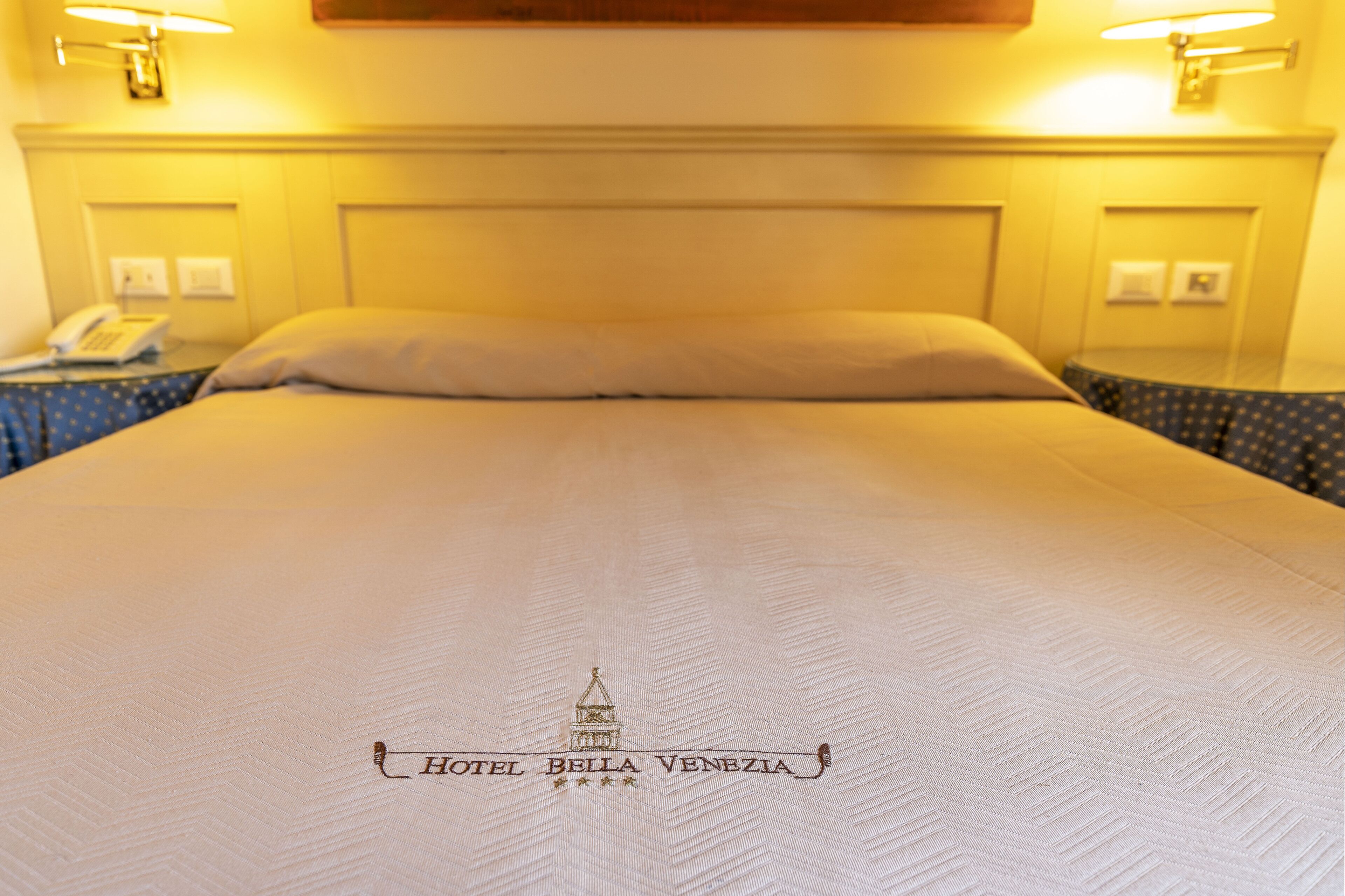 A hotel bed with a headboard, a pillow, and a logo on the bedspread.
