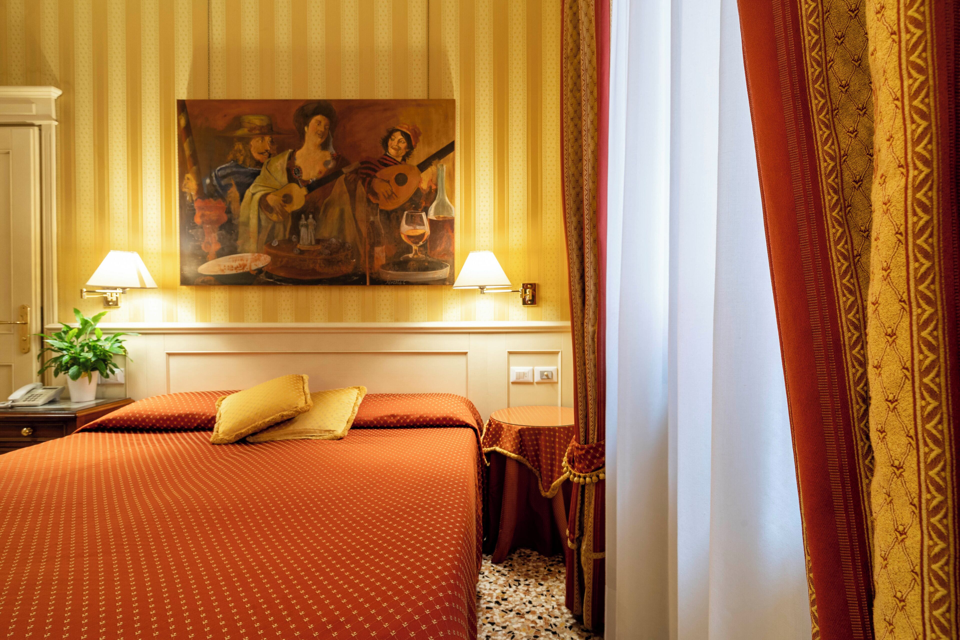 Habitación de hotel con una cama, dos lámparas de noche, un cuadro en la pared y una ventana con cortinas.
