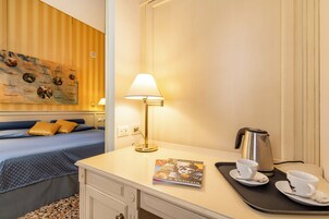 Una camera d'albergo con un letto, una scrivania con una lampada, una macchina del caffè e una rivista sul vassoio.