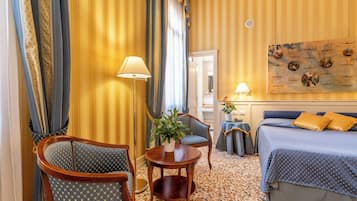 A hotel room with a bed, two armchairs, a small table with a plant, and a painting on the wall.