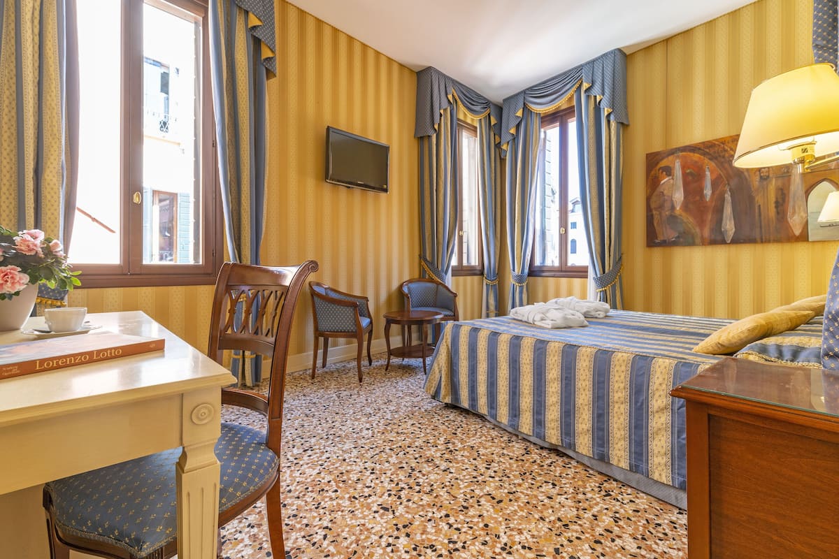Ein Hotelzimmer mit Bett, Schreibtisch, Stuhl, Fernseher und einem Bild an der Wand.