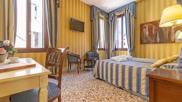 A hotel room with a bed, a desk, a chair, a television, and a painting on the wall.