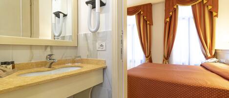 Camera d'albergo con lavabo doppio, uno specchio, un asciugacapelli, un letto con copriletto marrone e tende.