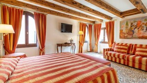 A hotel room with a wooden ceiling, two beds with striped bedding, a sofa, a TV, and a painting on the wall. - Hotel Bella Venezia (Venice)