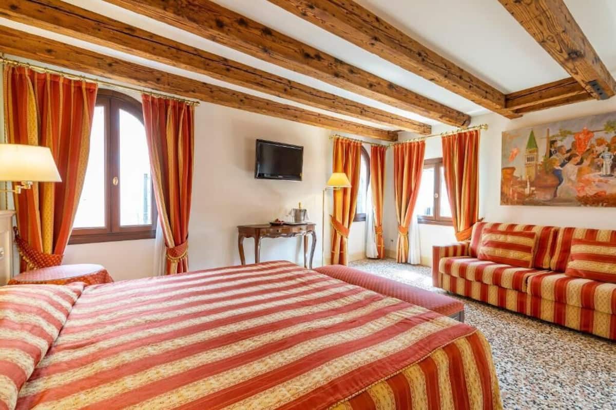 Ein Hotelzimmer mit Holzboden, zwei Betten mit gestreifter Bettwäsche, einem Sofa, einem Fernseher und einem Bild an der Wand.
