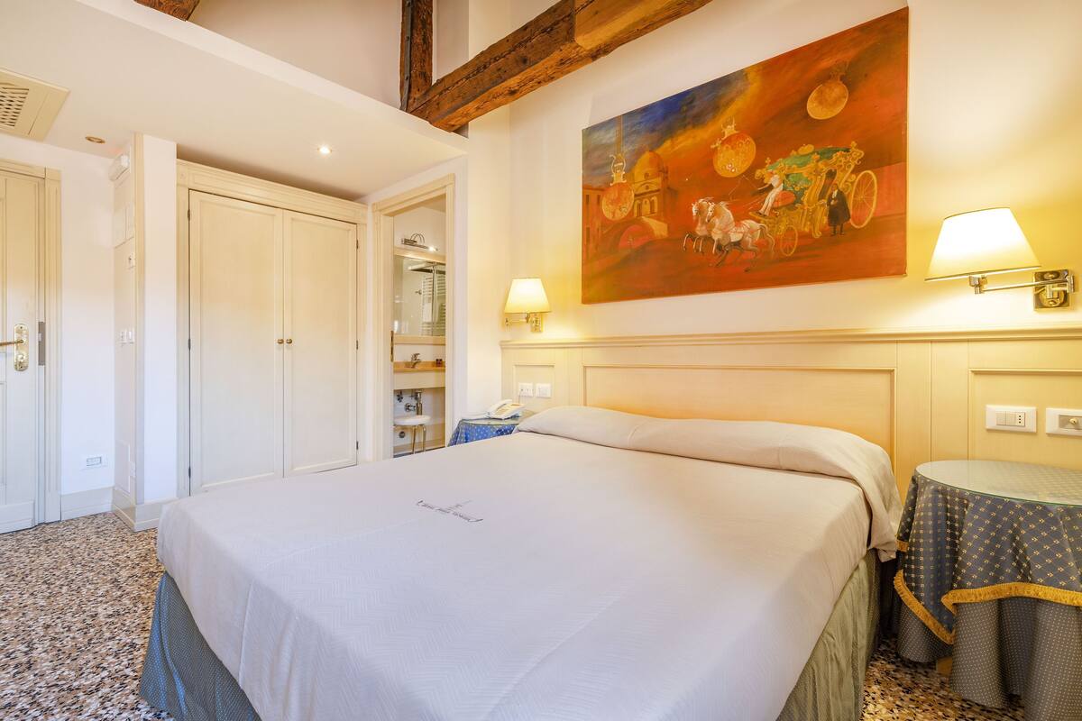 Ein Hotelzimmer mit Bett, einem Gemälde, einer Lampe und einem kleinen Tisch.