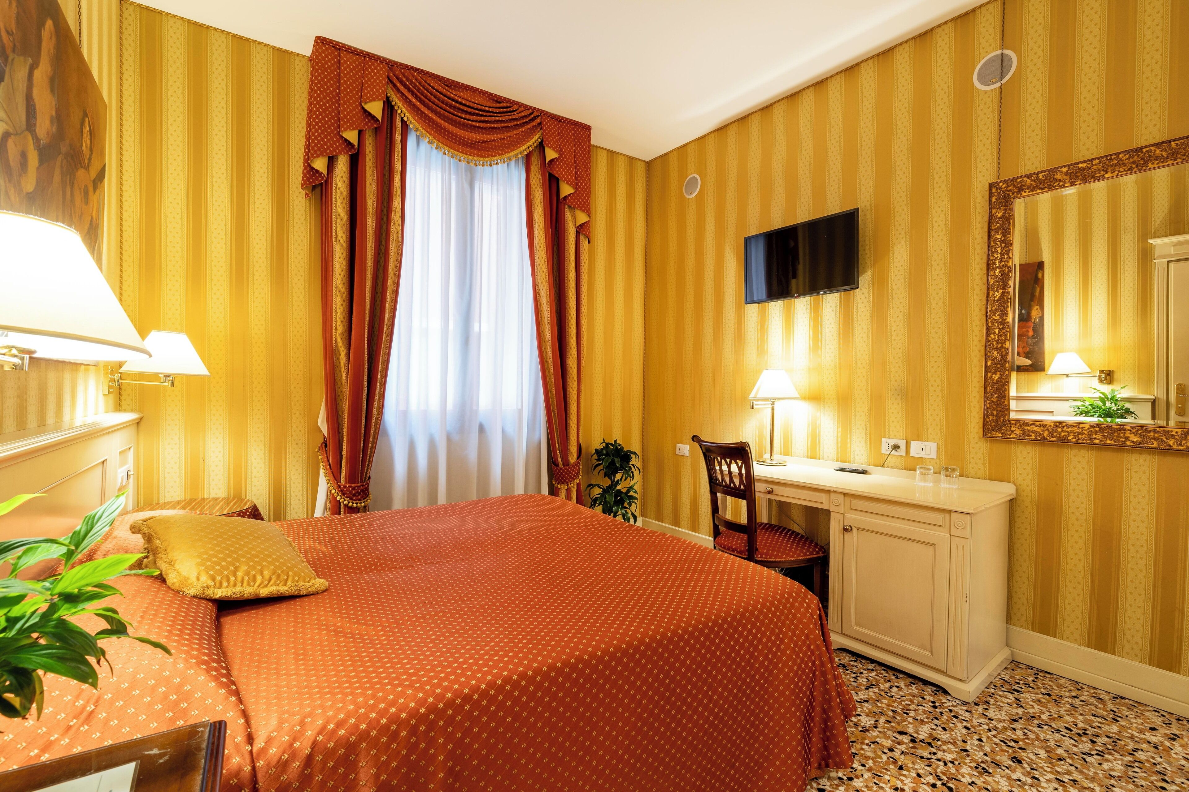 Habitación de hotel con cama, escritorio, silla y un espejo grande.