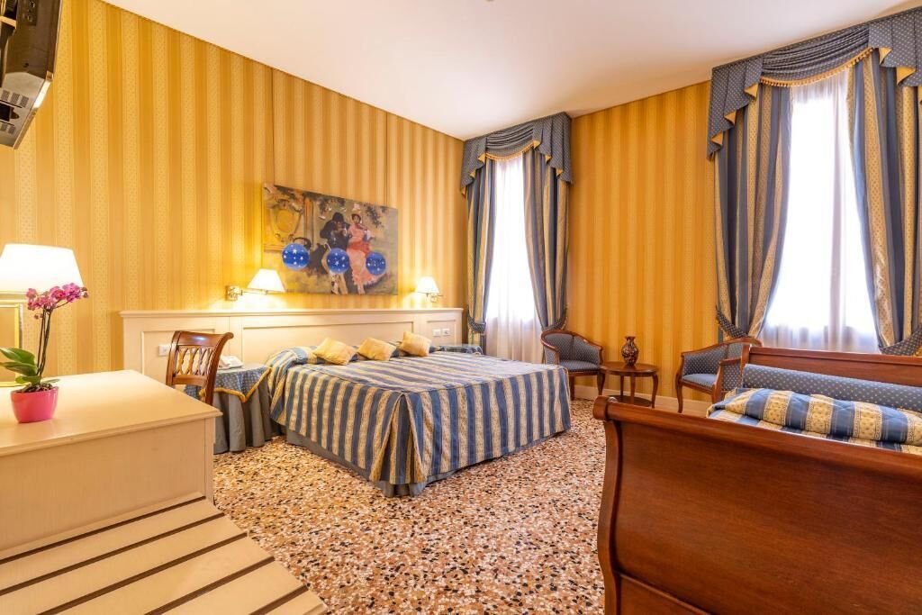 A hotel room with a large bed, two chairs, a small table, and a painting on the wall.