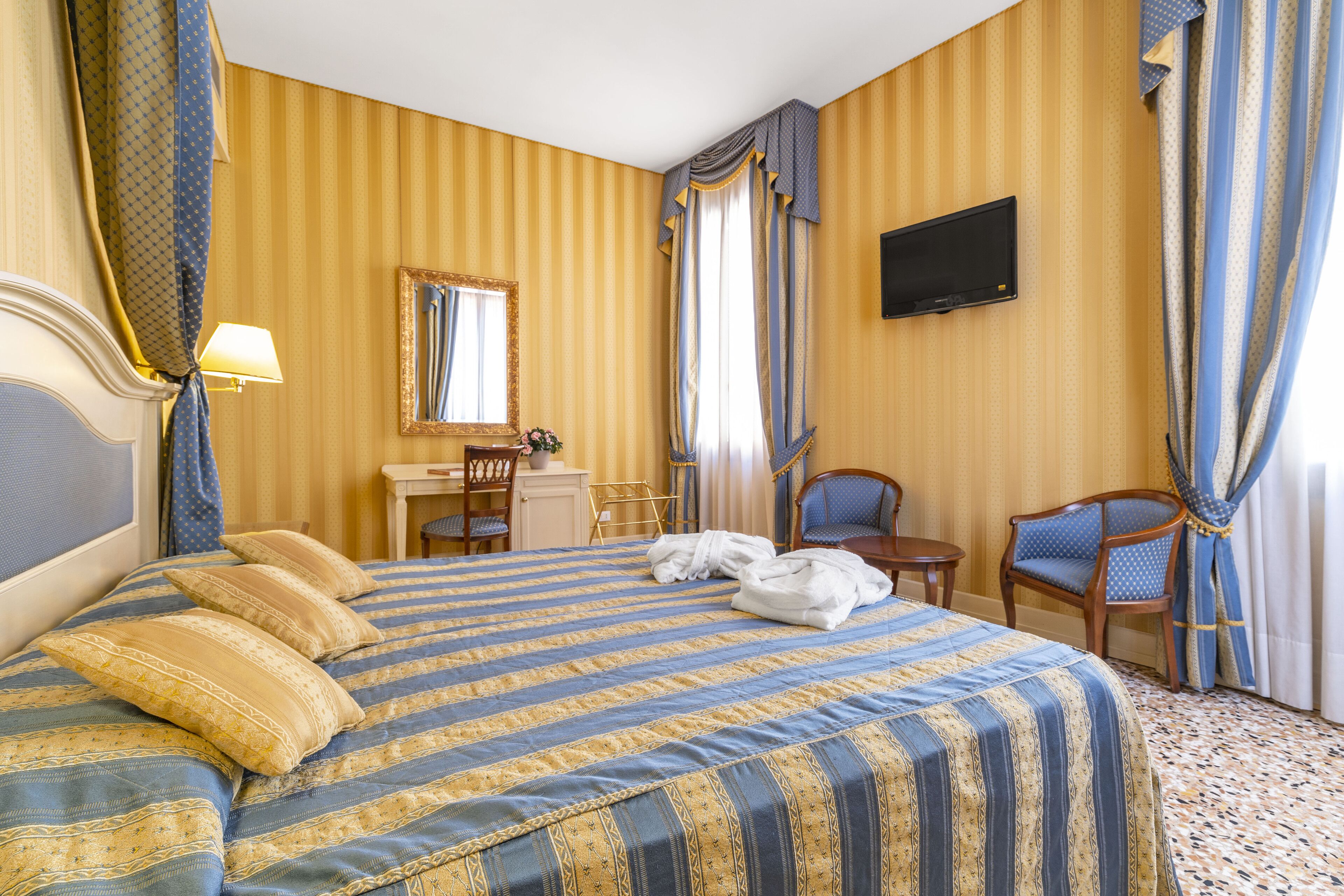 A hotel room with a large bed, a desk, a chair, and a television on the wall.