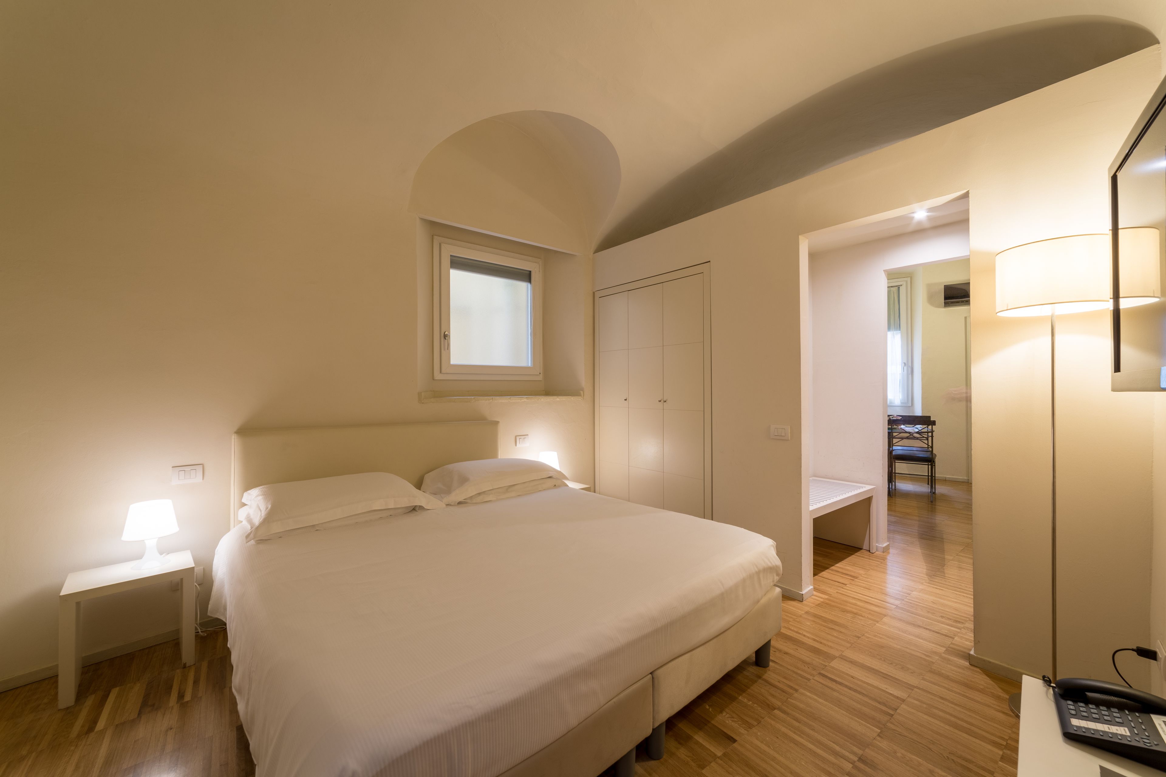 A bedroom with a bed, a nightstand, a lamp, a wardrobe, and a mirror.