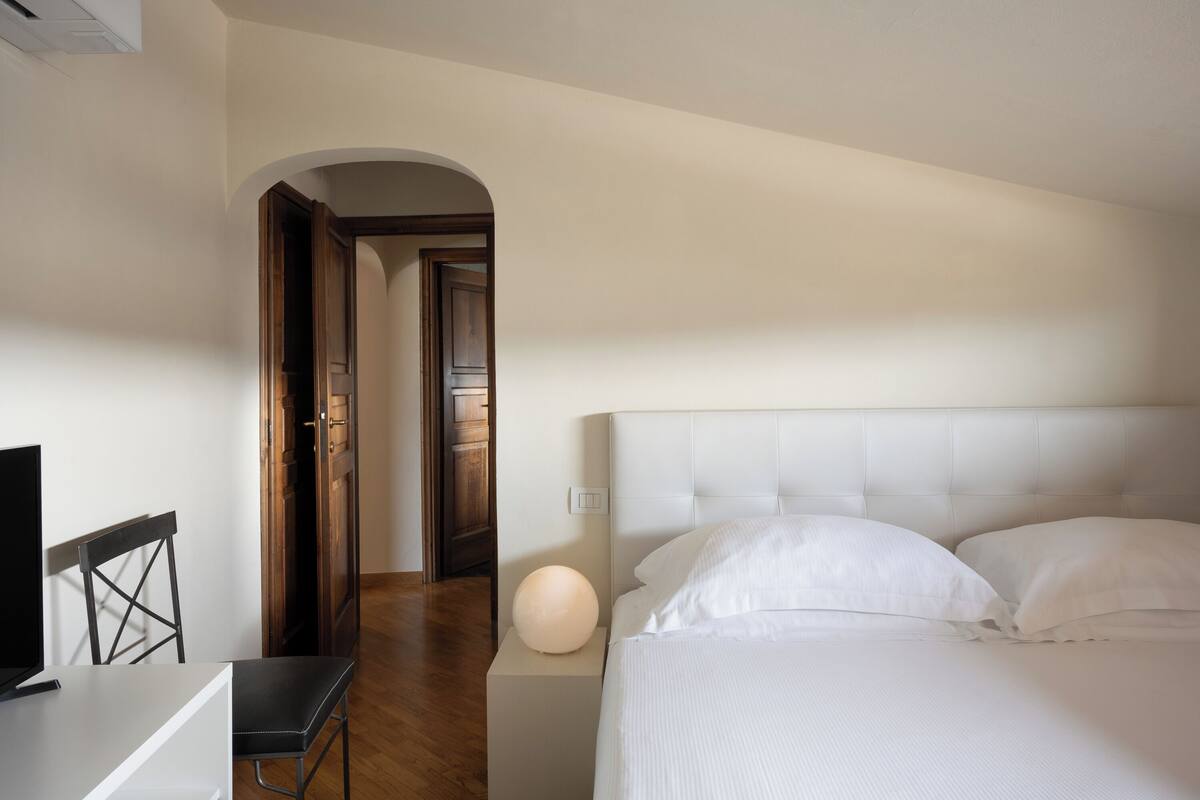 Une chambre à coucher avec un lit, un bureau et une chaise. Une porte donne accès à une autre pièce.