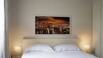 A hotel room with a bed, two bedside lamps, a painting of a cityscape, and a curtain on the left.