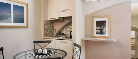 A compact kitchen with a dining area, featuring a round glass table, black chairs, and a tiled backsplash.