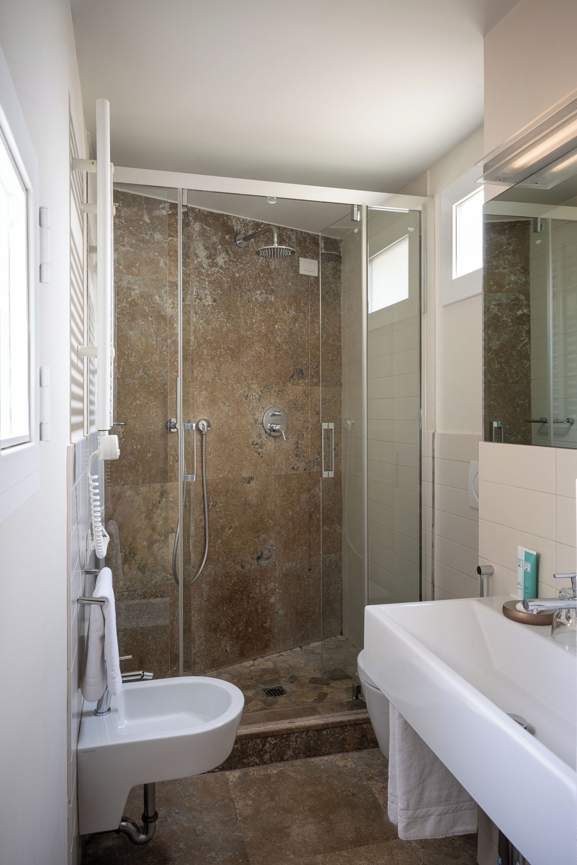 A modern bathroom with a glass-enclosed shower, a white sink, and a large mirror.
