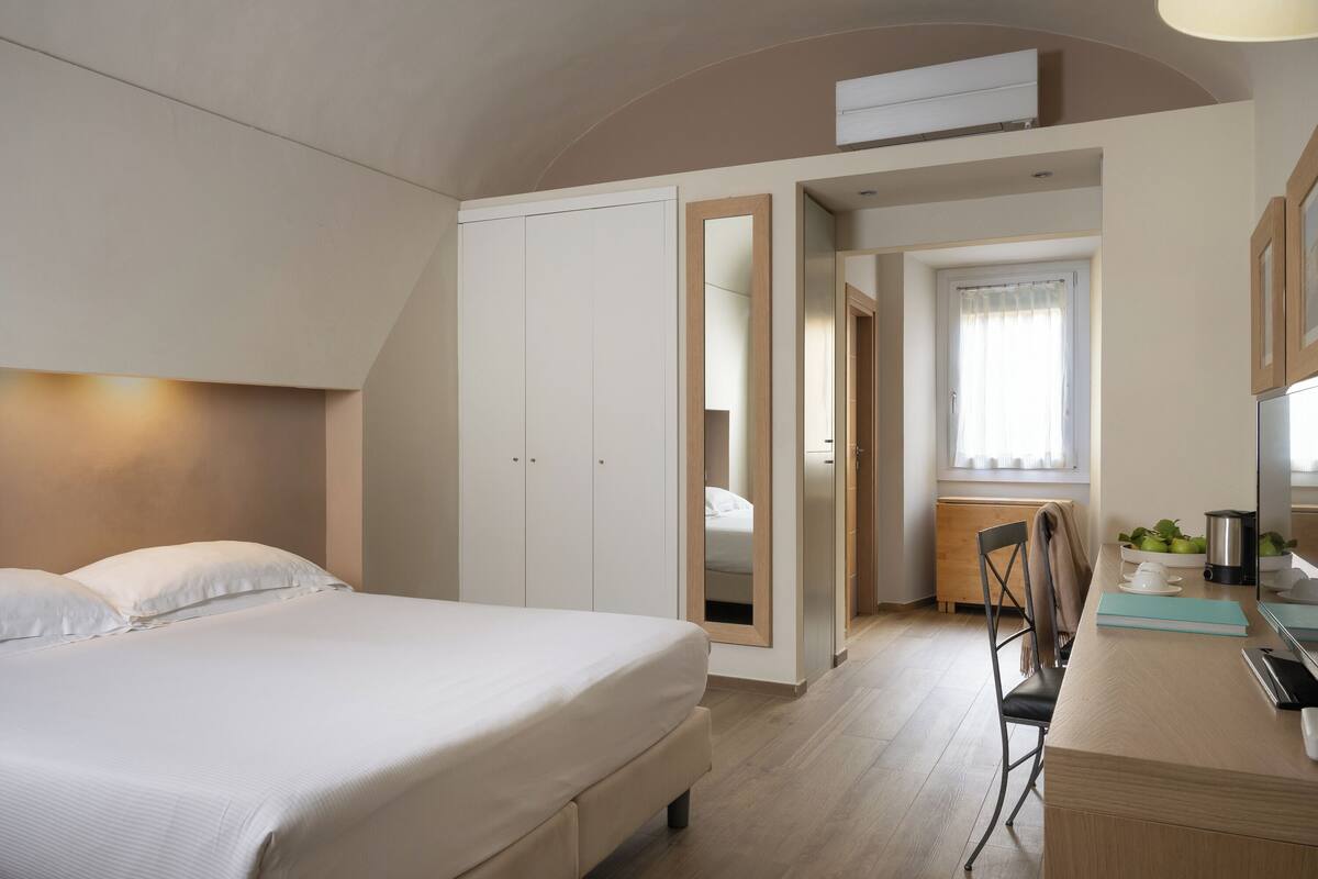 Une chambre à coucher avec un lit, un bureau et une chaise. On y trouve également une armoire et une fenêtre avec des rideaux.