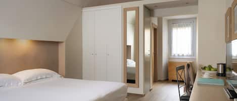 Un dormitorio con cama, escritorio y silla. Hay un armario y una ventana con cortinas.
