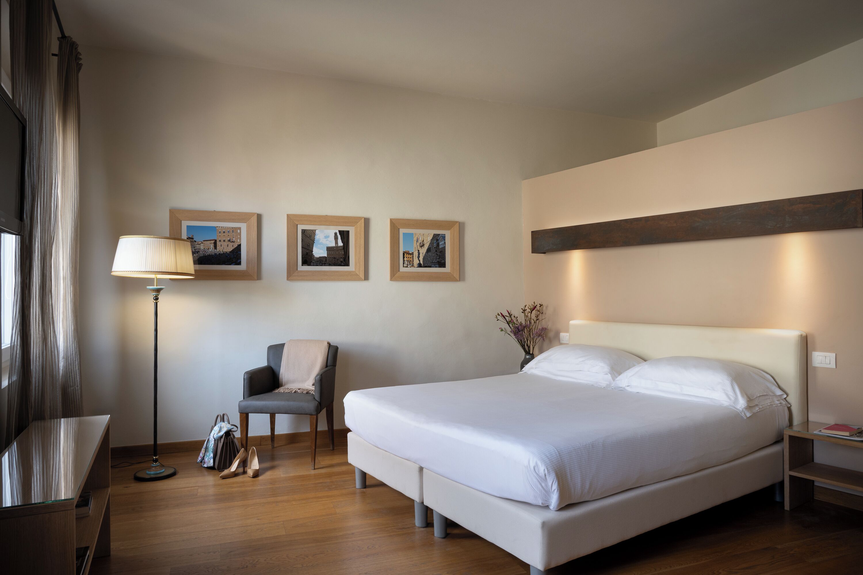 Une chambre d’hôtel avec un grand lit, un bureau, une chaise et une lampe sur pied. Trois tableaux encadrés sont accrochés au mur.