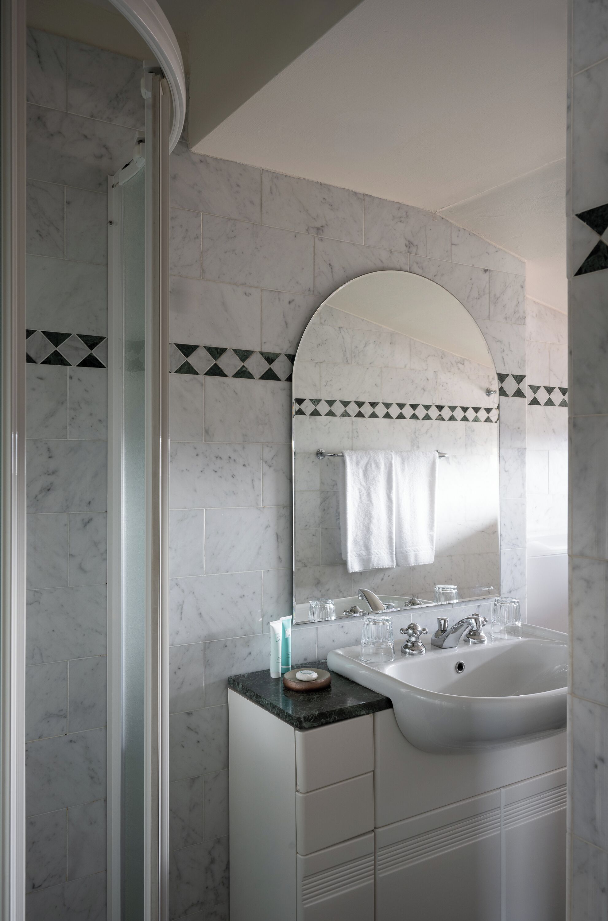 Une salle de bain dotée d’une douche à parois de verre, d’un lavabo blanc avec un plan de toilette en marbre et d’un grand miroir au-dessus du lavabo.