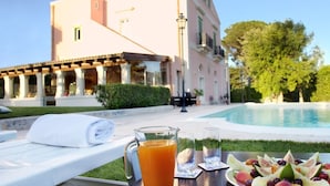A poolside setting with a lounge chair, a glass of orange juice, and a fruit platter.