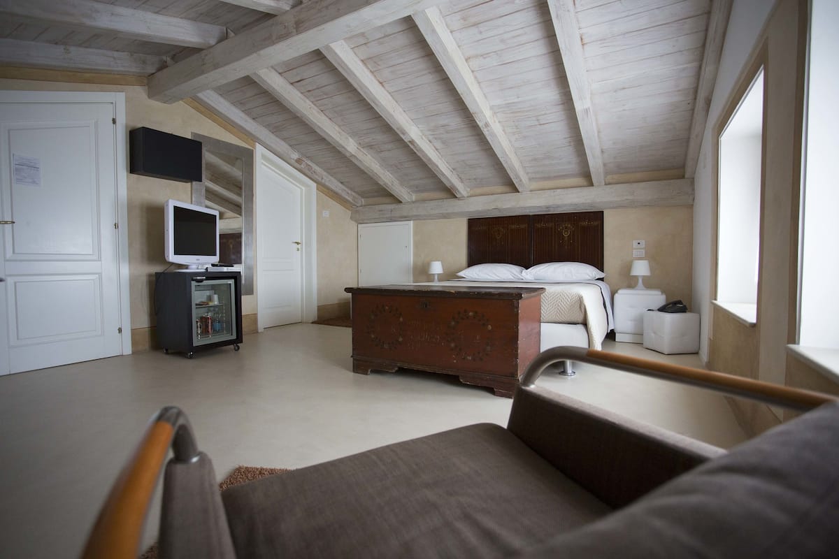A bedroom with a wooden ceiling, a bed, bedside tables, a dresser, a television, and a wardrobe.
