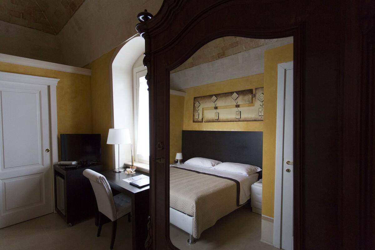 A hotel room with a bed, a desk with a computer, a chair, and a television.