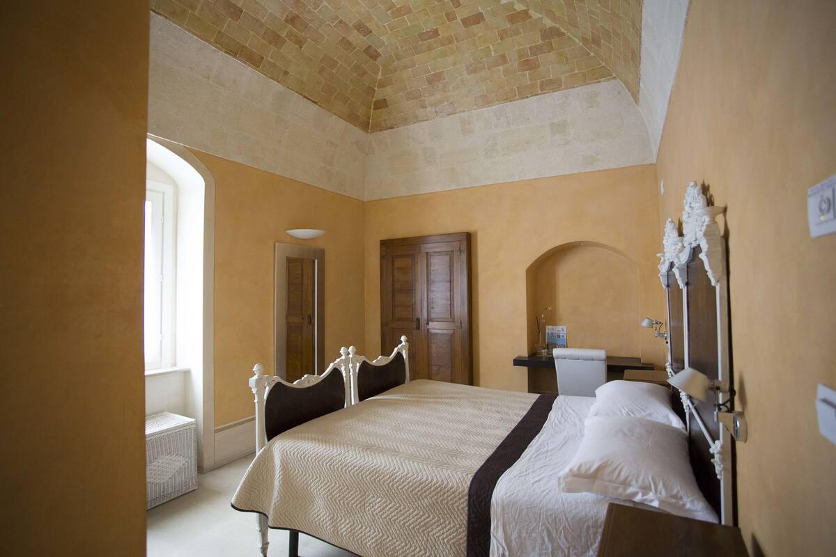 A bedroom with a large bed, wooden headboard, and a brick ceiling.