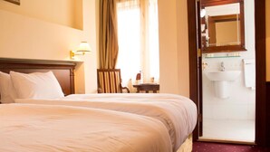 A hotel room with a large bed, a chair, a small table, a bathroom with a sink and mirror, and a door leading to the bathroom. - Stone Bridge Hotel (Skopje)