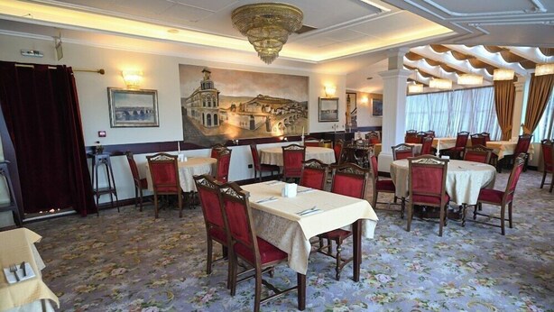 A dining area with tables set for four, red upholstered chairs, and a floral carpet. - Stone Bridge Hotel (Skopje)