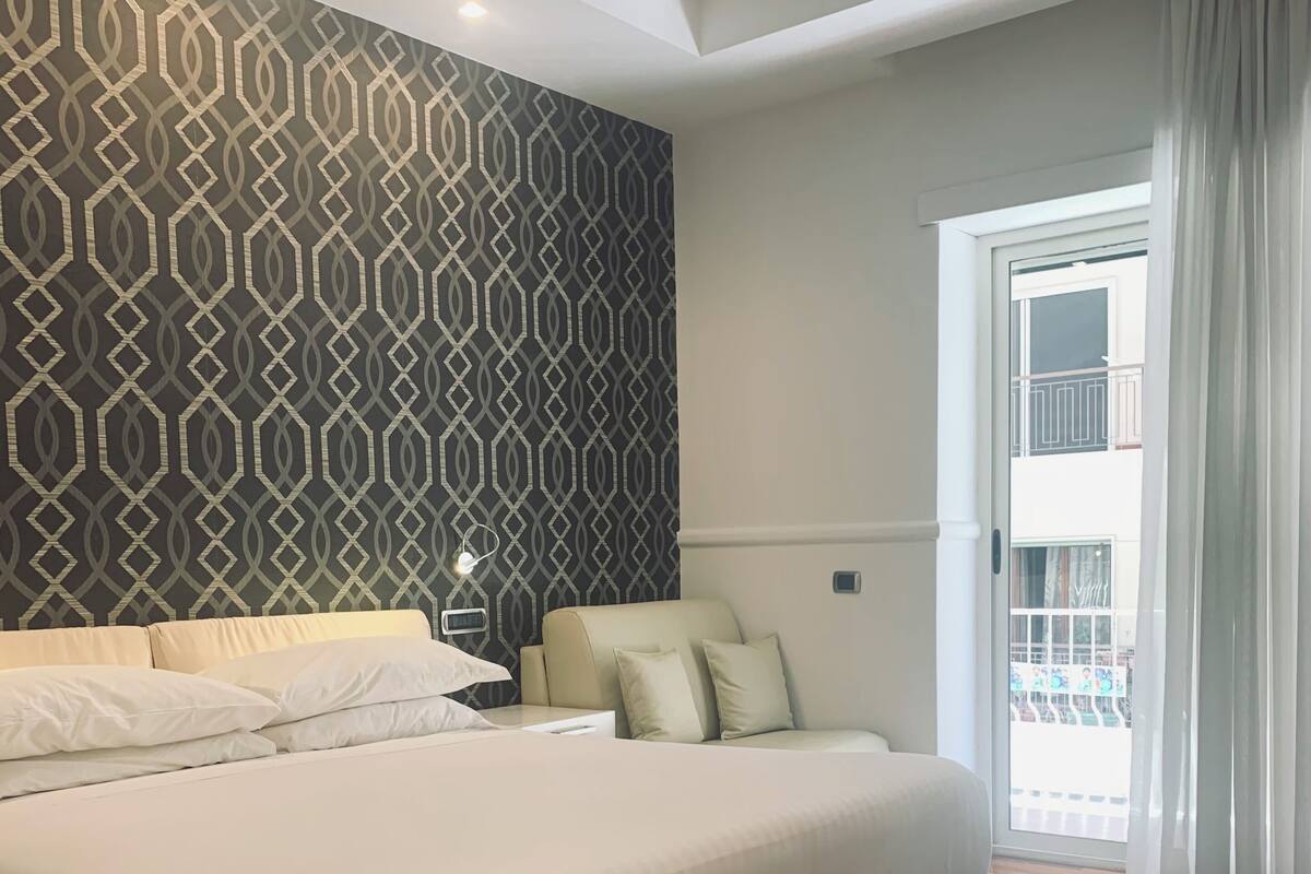 A bedroom with a large bed, a nightstand, and a view of the outside through a door.