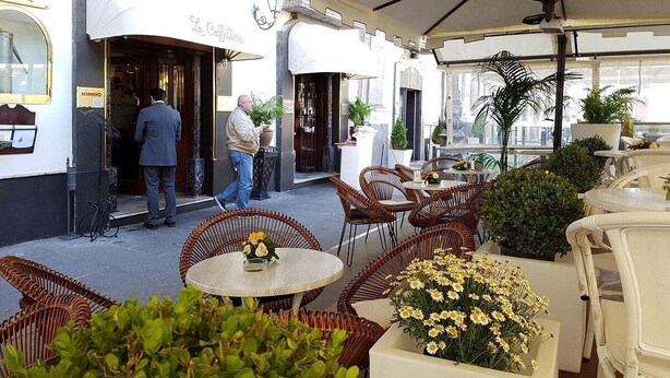 An outdoor cafe with wicker furniture and potted plants.