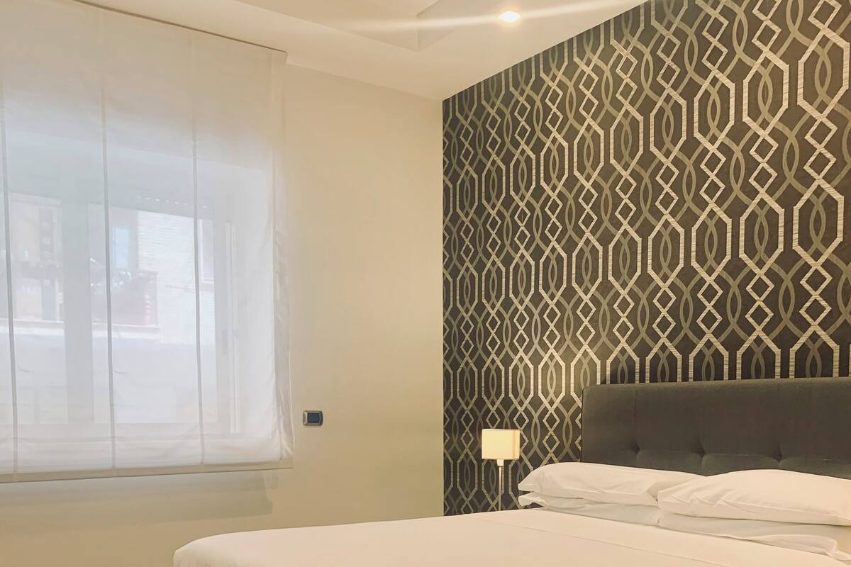A bedroom with a bed, a patterned wall, and a window with curtains.