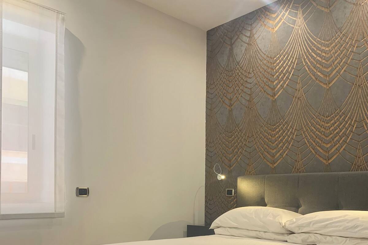 A modern bedroom with a large bed, a patterned wall, and a wooden floor.