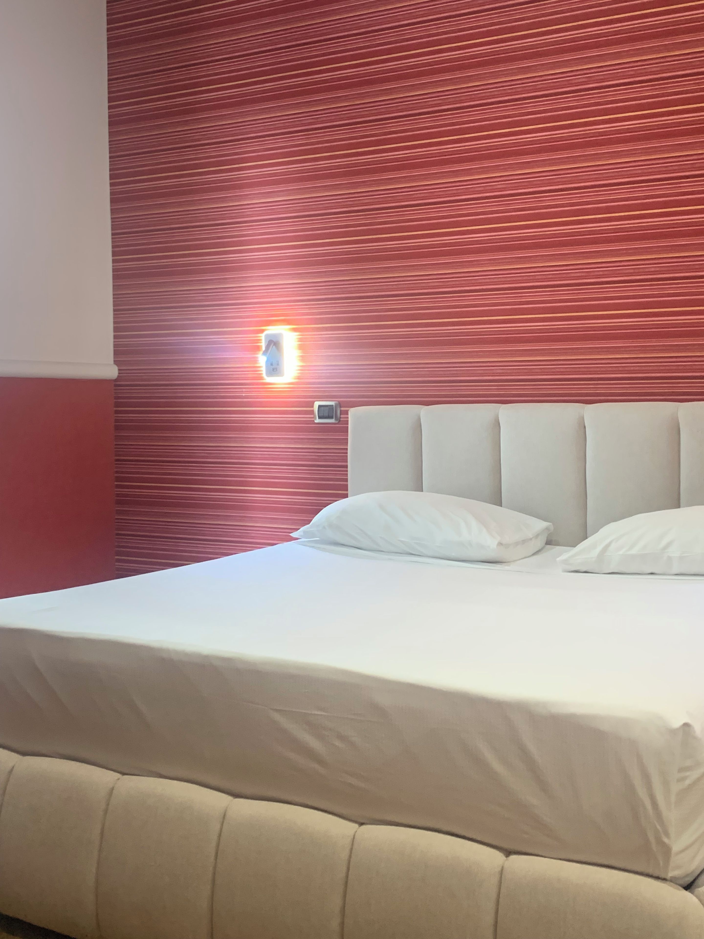 A bed with a headboard, white bedding, and a wall with a red pattern.