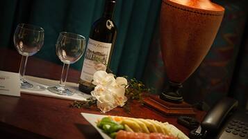 Una mesa con una botella de vino, dos copas, un plato de comida, un teléfono y una lámpara decorativa.