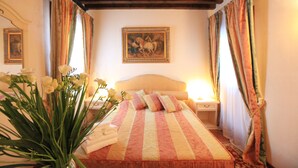 A bedroom with a bed, a nightstand, a vase with flowers, and a painting on the wall. - Residenza Giardini (Venice)