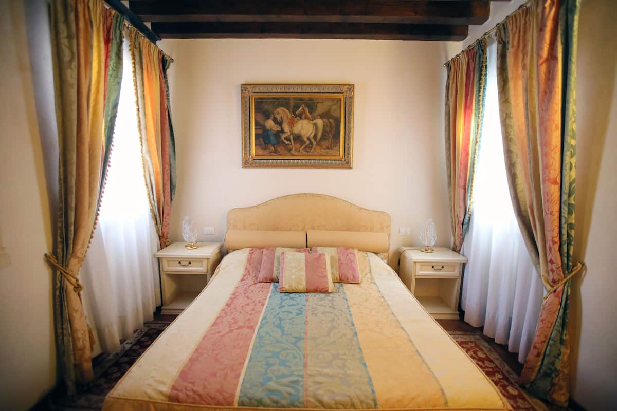 A bedroom with a large bed, two bedside tables, a headboard, and curtains.