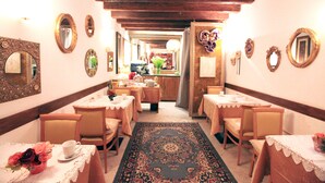 A hotel corridor with multiple dining tables and chairs, ornate mirrors, and a patterned carpet. - Residenza Giardini (Venice)