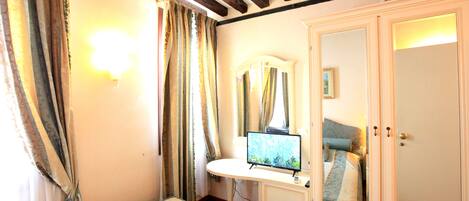 A bedroom with a bed, a desk with a computer, a wardrobe, and a mirror.