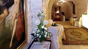 Una habitación con pared de piedra, un cuadro, un jarrón con flores y una cama con alfombra.