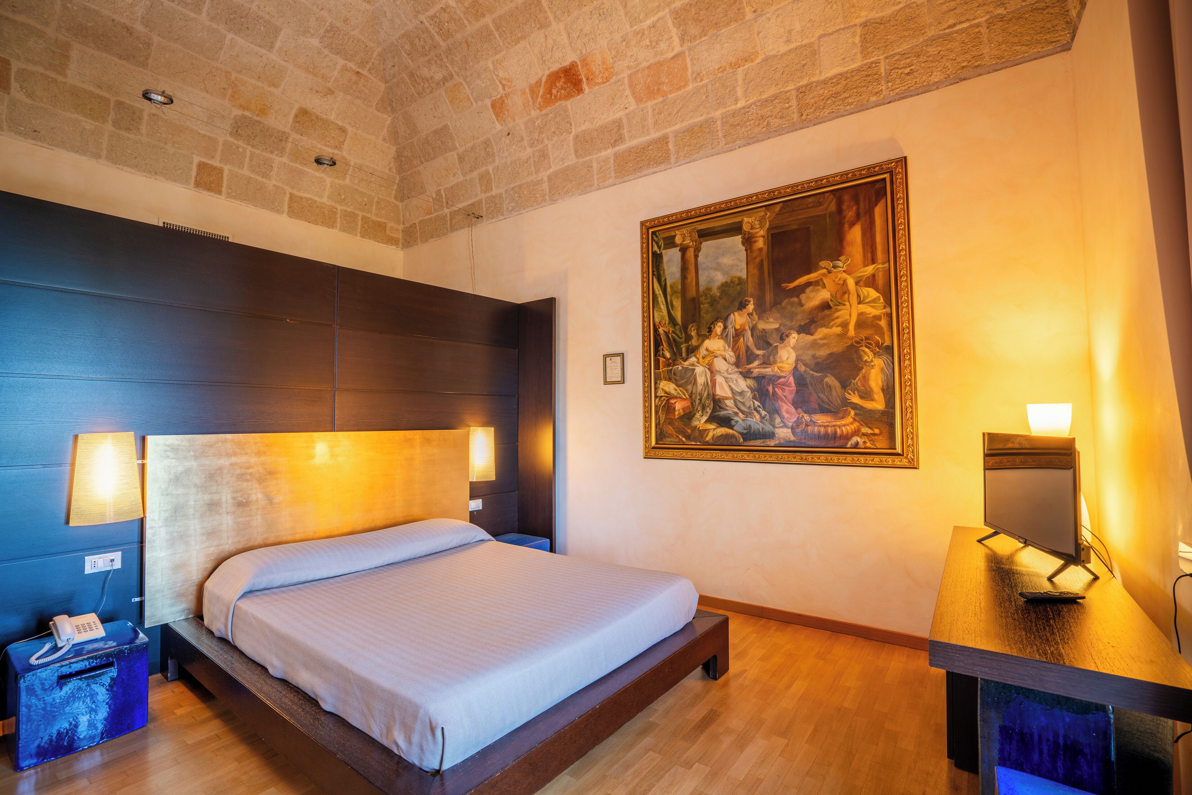 A modern hotel room with a large bed, a desk, and a painting on the wall.